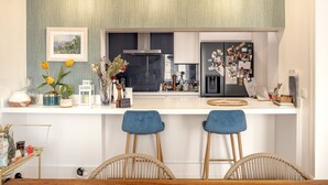 Eine moderne Küche mit weißer Arbeitsplatte, blauen Barhocker und einer hängenden Leuchte.