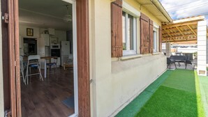 An open door leading to a kitchen with a dining area, a patio with artificial grass, and a wooden pergola.