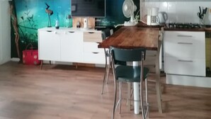 A modern kitchen with a wooden dining table, white cabinets, a large wall mural of a forest, and a clock on the wall.