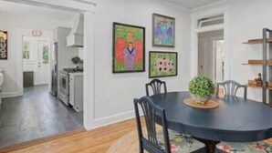 Un comedor con una mesa redonda, sillas y una planta en maceta. En la pared, se observan obras de arte enmarcadas.