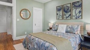 Un dormitorio con cama, mesitas de noche, un espejo y una obra de arte floral en la pared.
