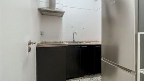 A compact kitchen with a stainless steel refrigerator, a sink, and black cabinets. - Estrela House III by Homing (Lisbon)