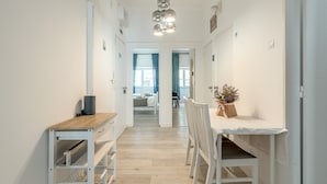 Un couloir doté d’un plancher en bois, de murs blancs, d’une table blanche avec des chaises et d’un luminaire suspendu.