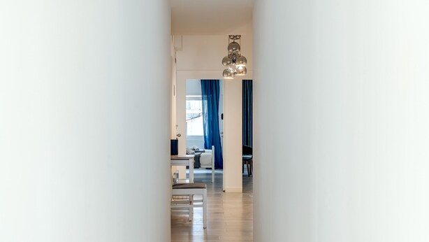 A hallway leading to a living area with a modern chandelier, a dining table, and blue curtains. - Estrela House IV by Homing (Lisbon)