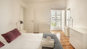Habitación de hotel con cama, mesita de noche, lámpara, radiador y ventana con vistas.