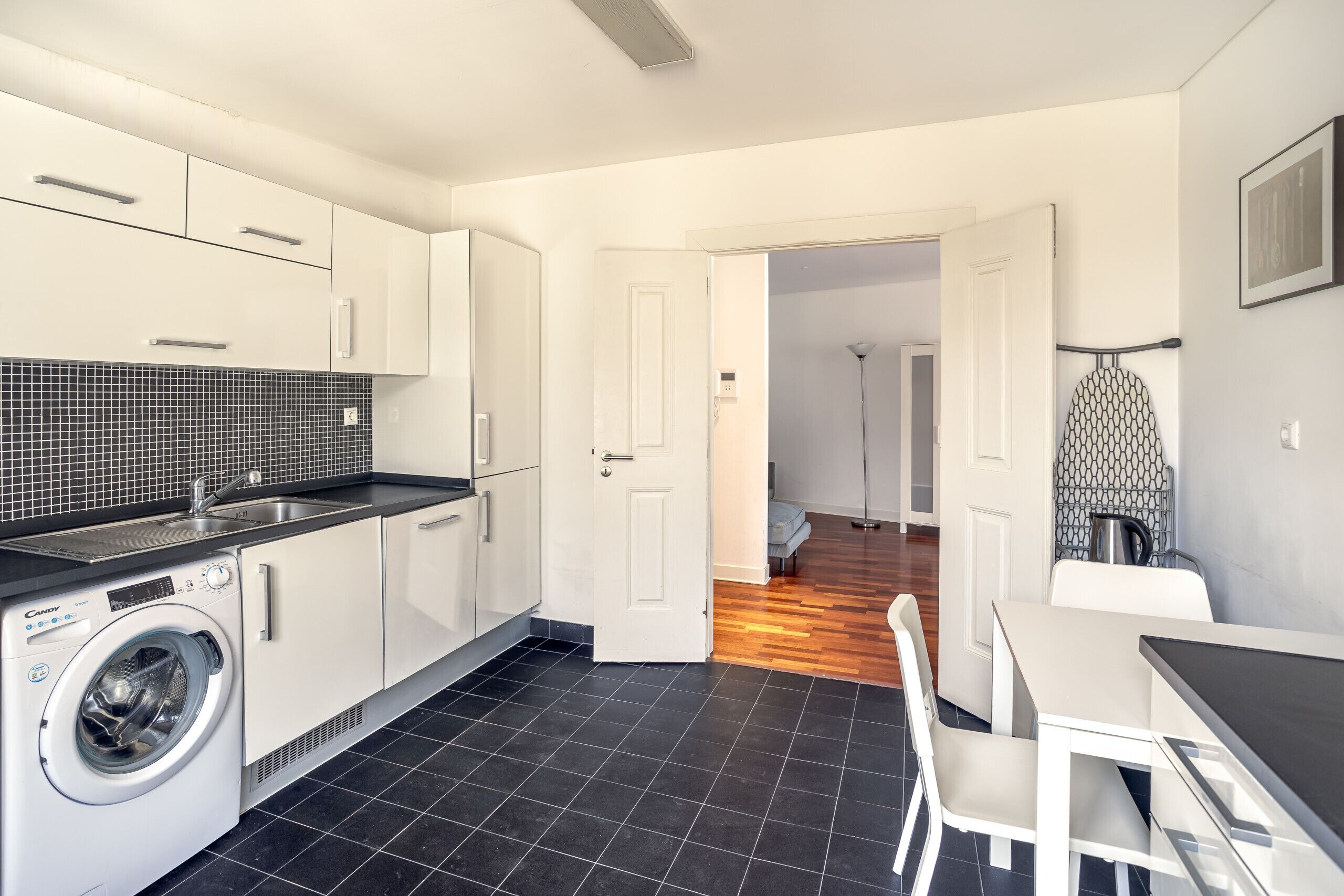 A modern kitchen with a washing machine, a dining area with a table and chairs, and a hallway leading to another room.