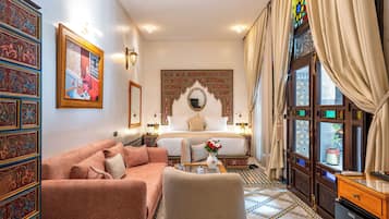Quarto tradicional com cama, sofá, espelho decorativo e vista pela janela com cortinas.