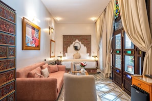 A traditional room with a bed, a sofa, a decorative mirror, and a view through a window with curtains. - Riad Joy (Fes)