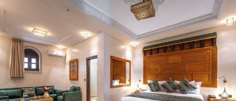 A hotel room with a large bed, a sofa, a small table, and a decorative headboard.