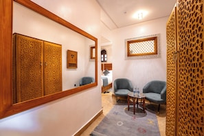 A hallway with a large mirror, two chairs, a small table with a bottle, and a decorative wall panel. - Riad Joy (Fes)