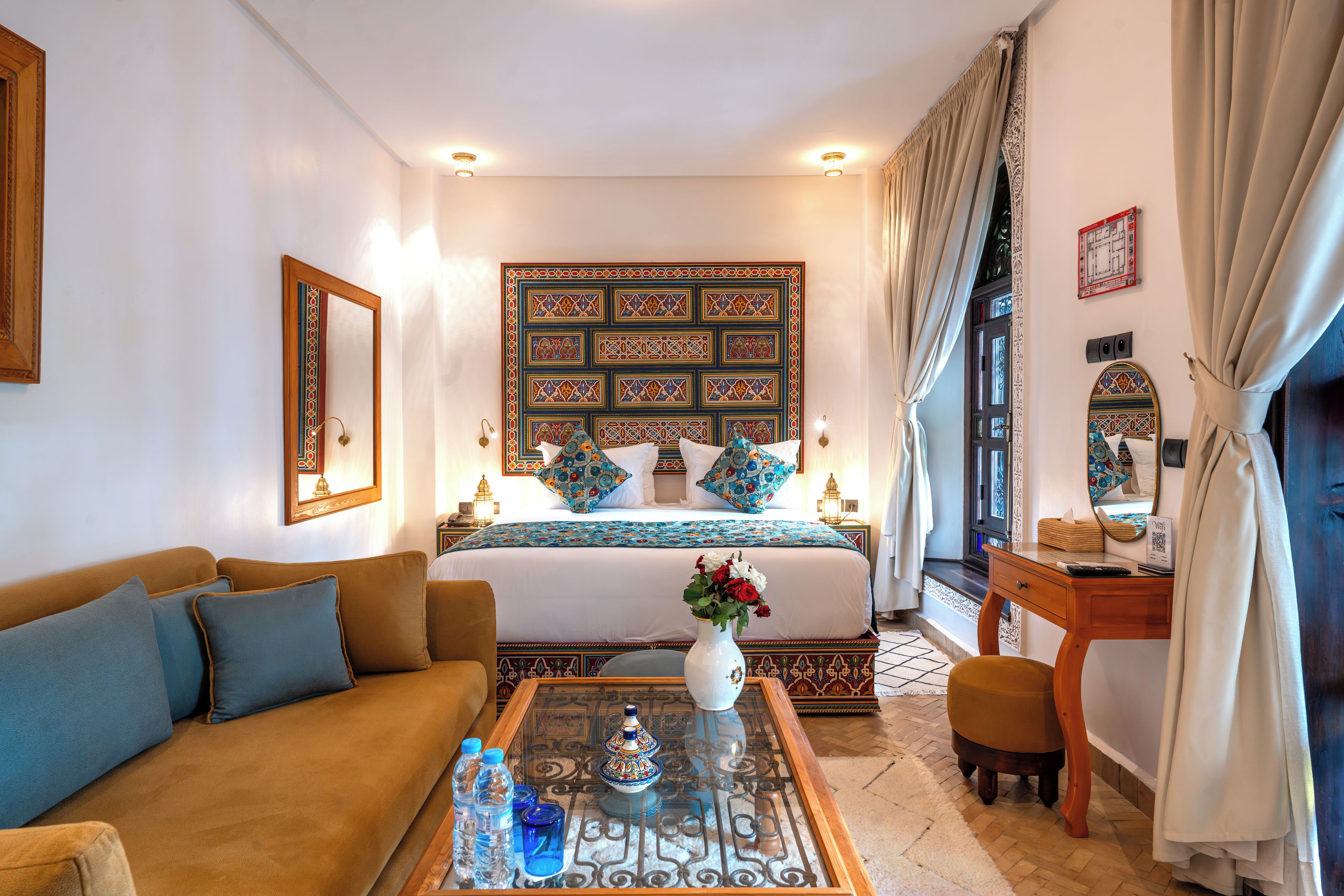A hotel room with a bed, a sofa, a coffee table with decorative items, and a desk with a lamp.