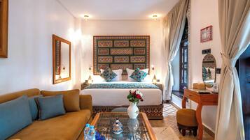 A hotel room with a bed, a sofa, a coffee table with decorative items, and a desk with a lamp.