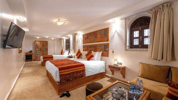 Habitación de hotel con dos camas, un sofá, una mesa de centro y un televisor.