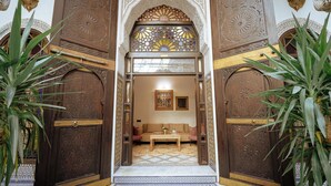 An ornate doorway with intricate carvings, leading into a room with a patterned floor and a sofa. - Riad Joy (Fes)
