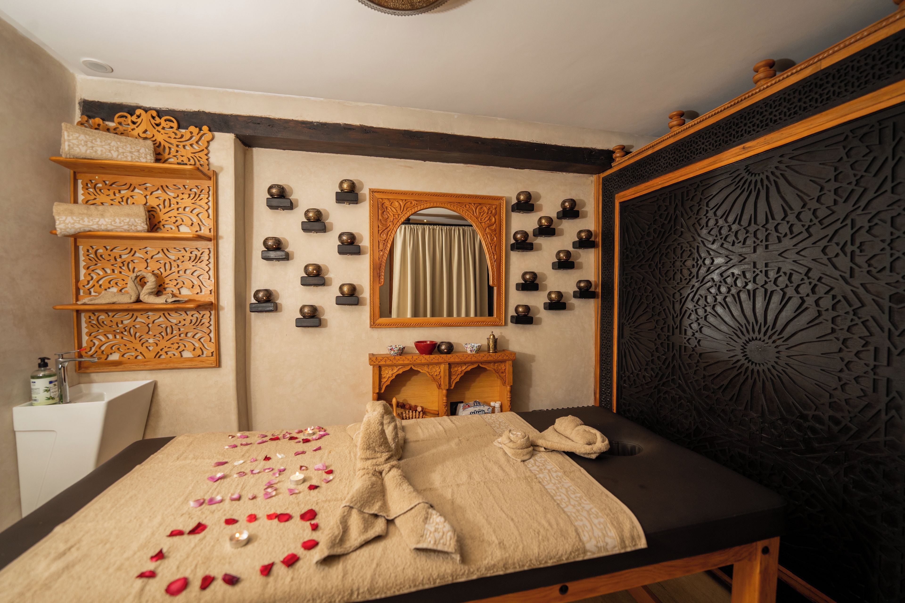 A room with a bed, a wooden shelf with towels, a mirror, and a decorative wall panel.