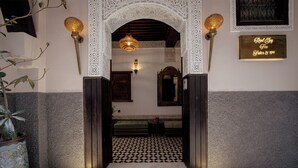 A traditional Moroccan-style entrance with intricate white arches, a checkered tile floor, and a sign indicating a Riad Toy Fes hotel offering rooms and spa services. - Riad Joy (Fes)