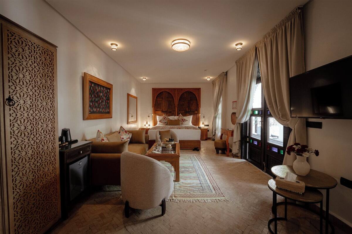 A hotel room with a bed, a sofa, a desk, a TV, and a decorative wall panel.