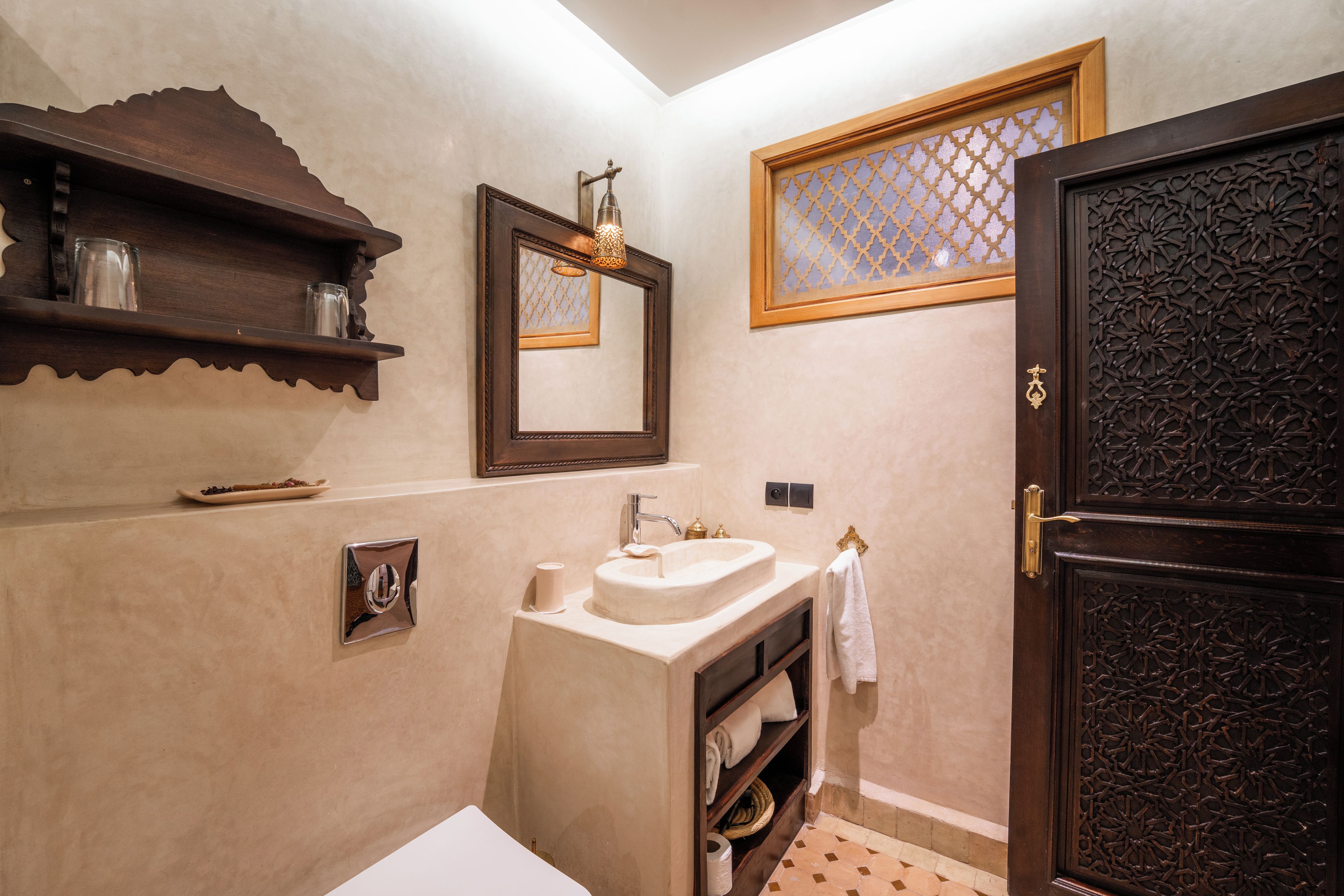 A bathroom with a sink, mirror, shelf, and decorative door.