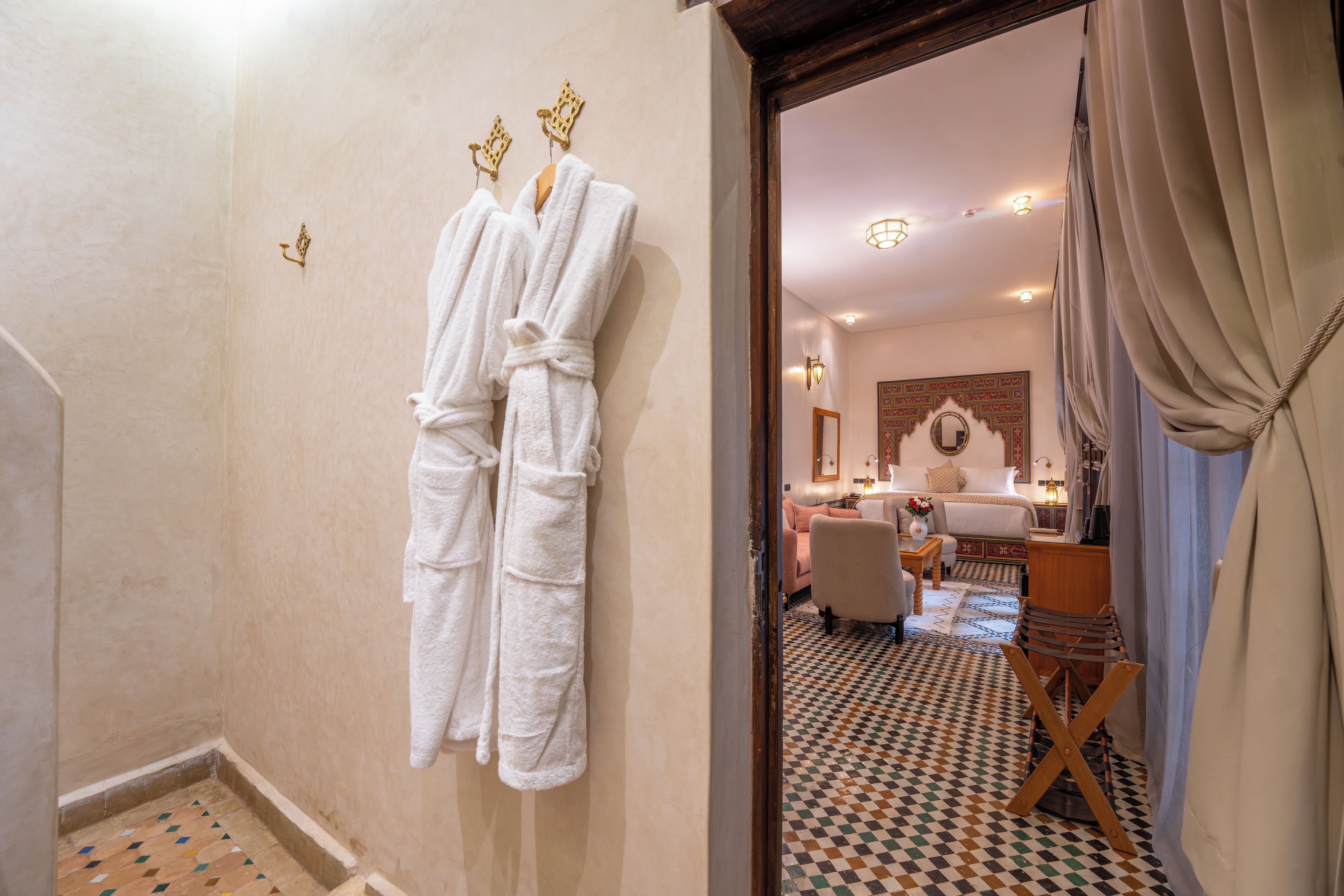 A hotel room with a checkered floor, a bed, a sitting area, and a bathroom with a towel rack.