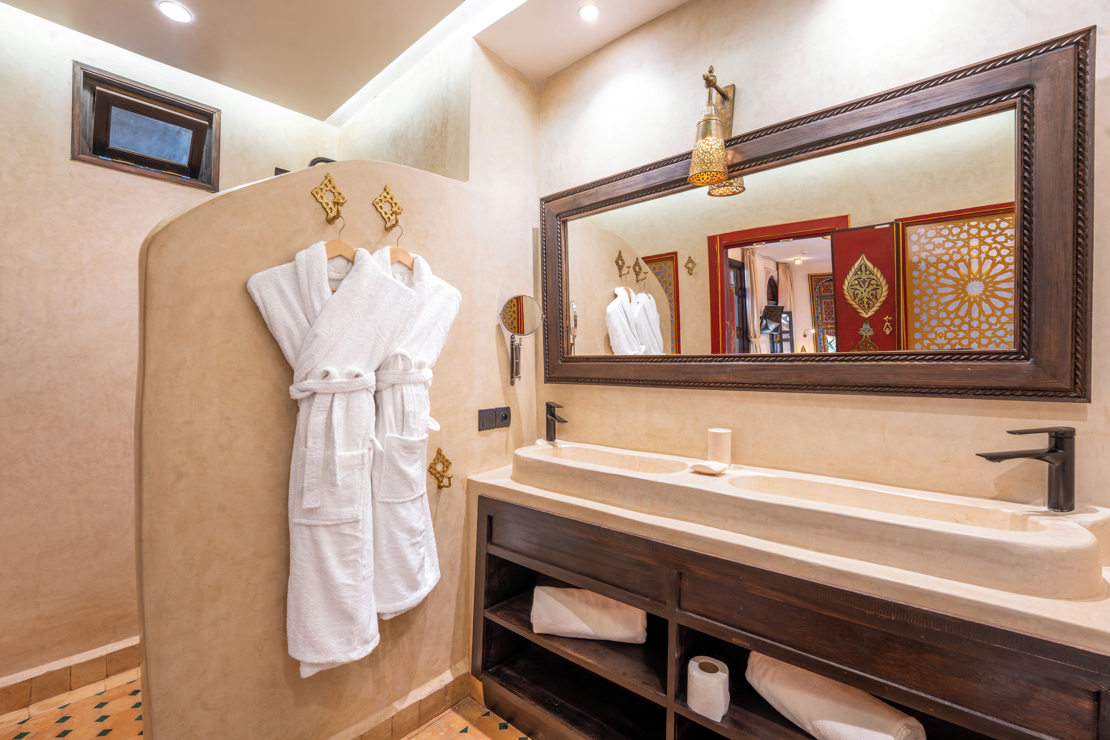 Une salle de bain avec un grand miroir, un lavabo et deux serviettes blanches suspendues à des crochets.