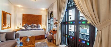 A hotel room with a bed, a sofa, a small table, a window with curtains, and a decorative wall panel.