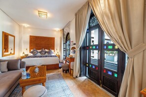 A hotel room with a bed, a sofa, a small table, a window with curtains, and a decorative wall panel. - Riad Joy (Fes)