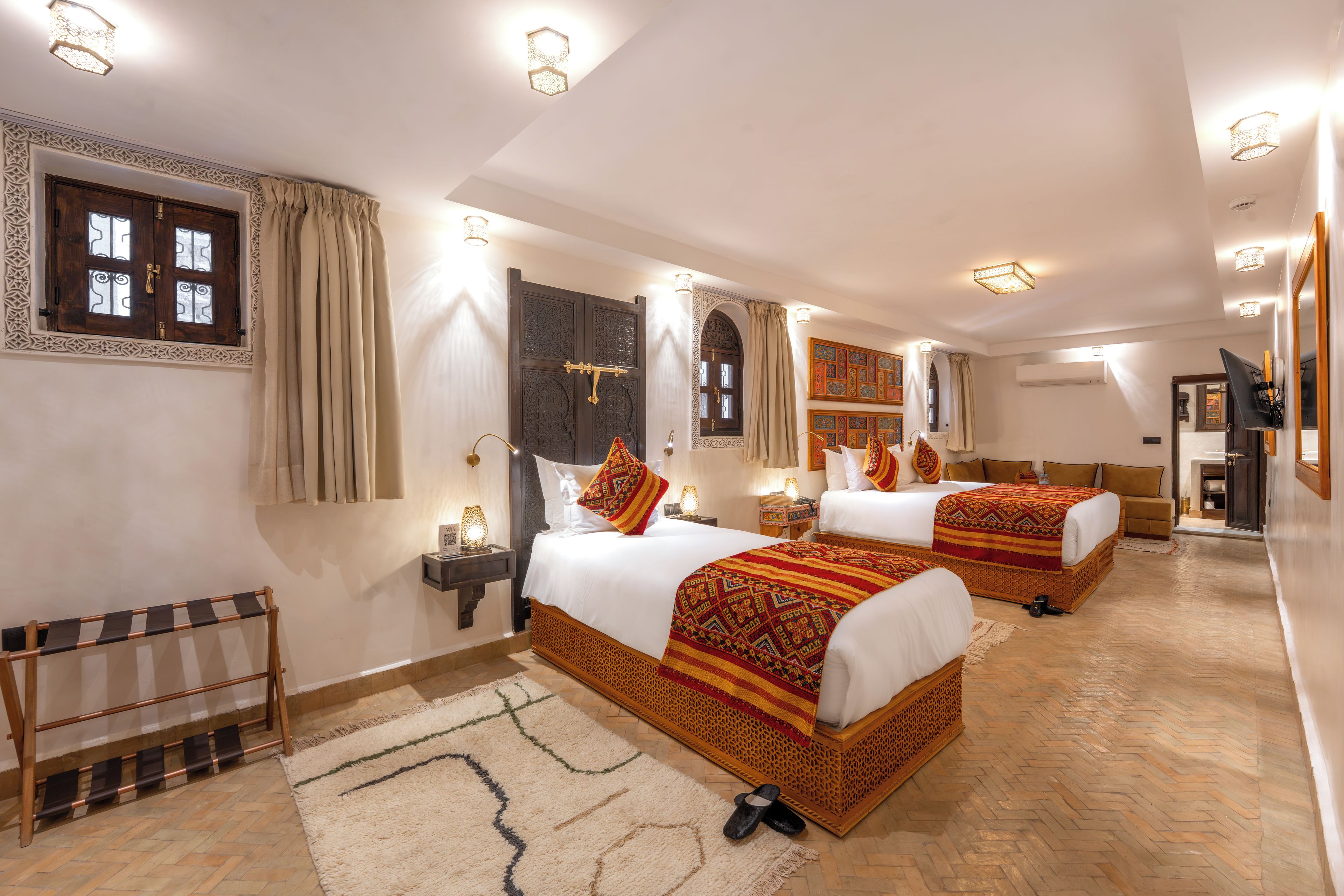 Ein Hotelzimmer mit zwei Betten, Holzboden, einem großen Spiegel und einem Fenster mit Vorhängen.