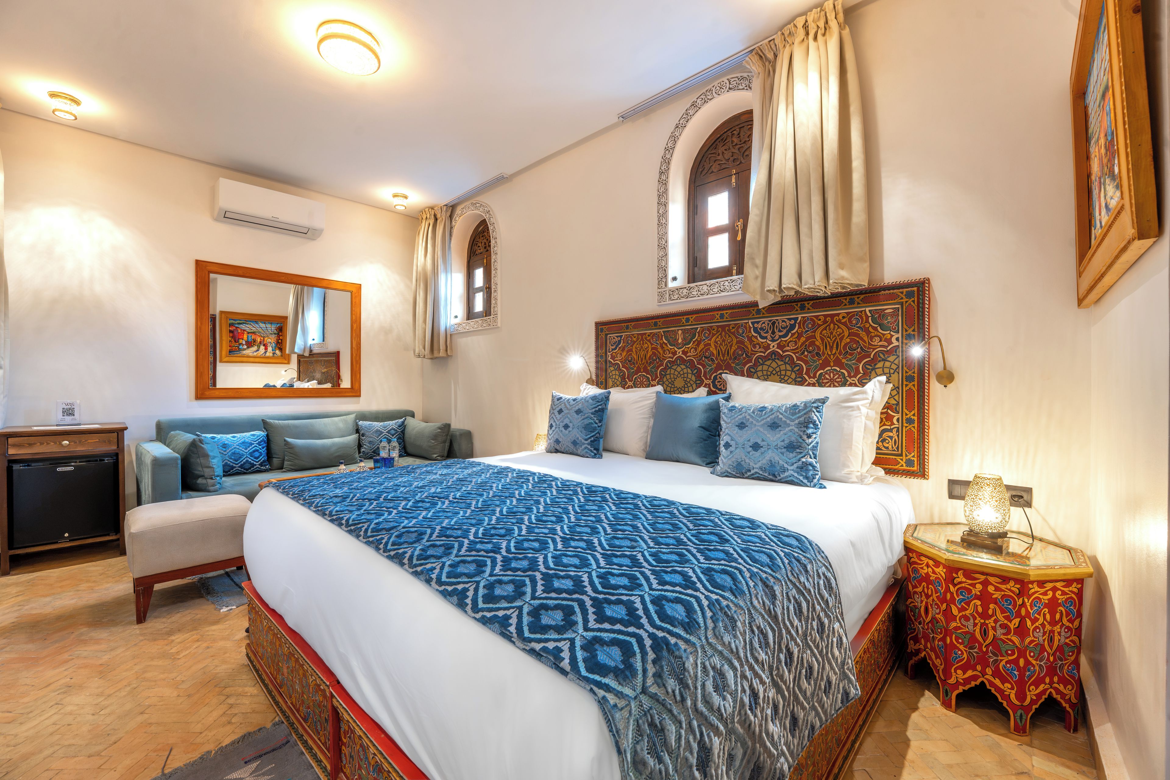 A hotel room with a large bed, a sofa, a small table, and a nightstand.