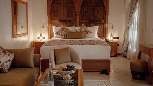 A spacious bedroom with a large bed, ornate wooden headboard, and a decorative wall panel. - Riad Joy (Fes)