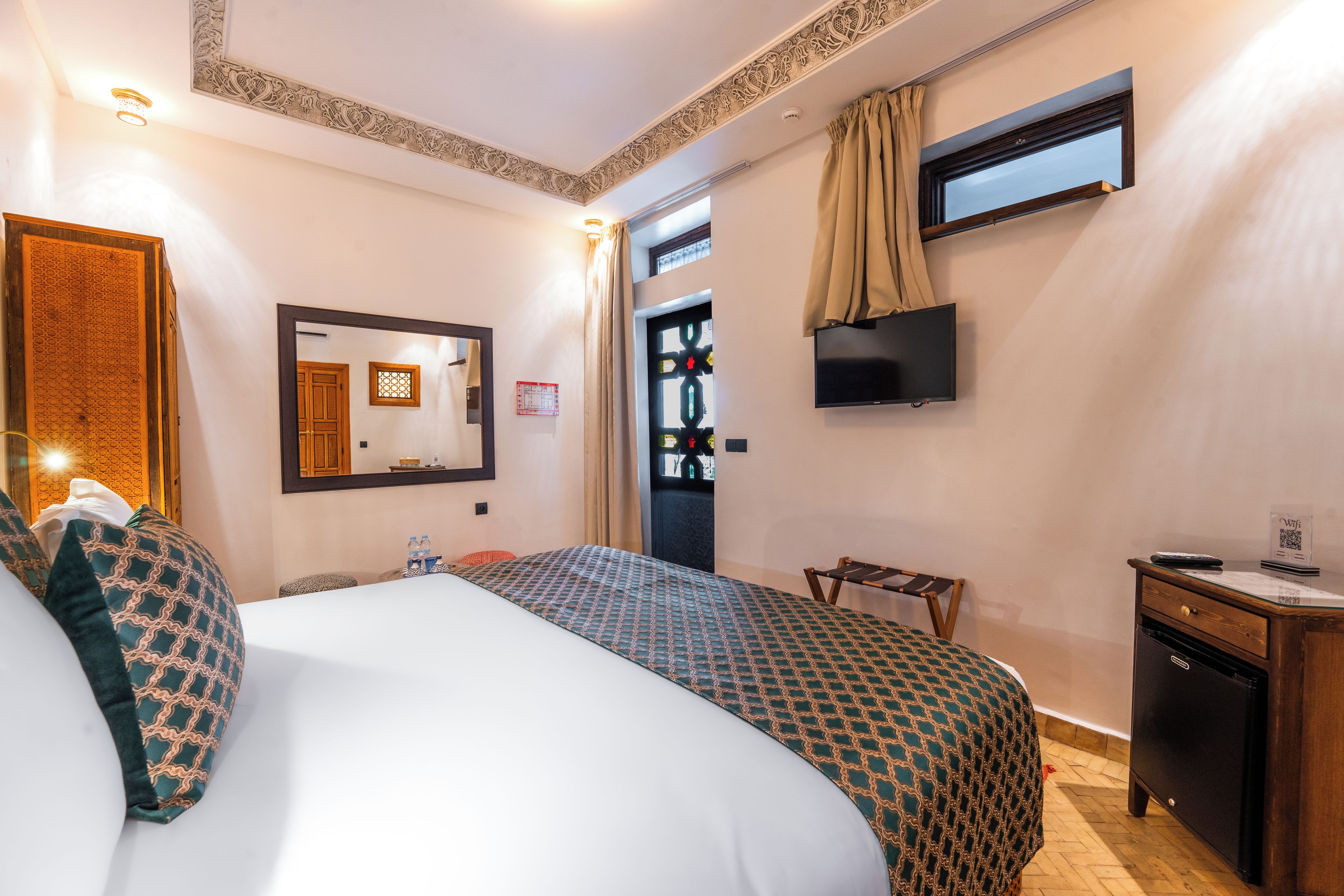 Une chambre d’hôtel avec un lit, un bureau, une télévision et une fenêtre avec des rideaux.