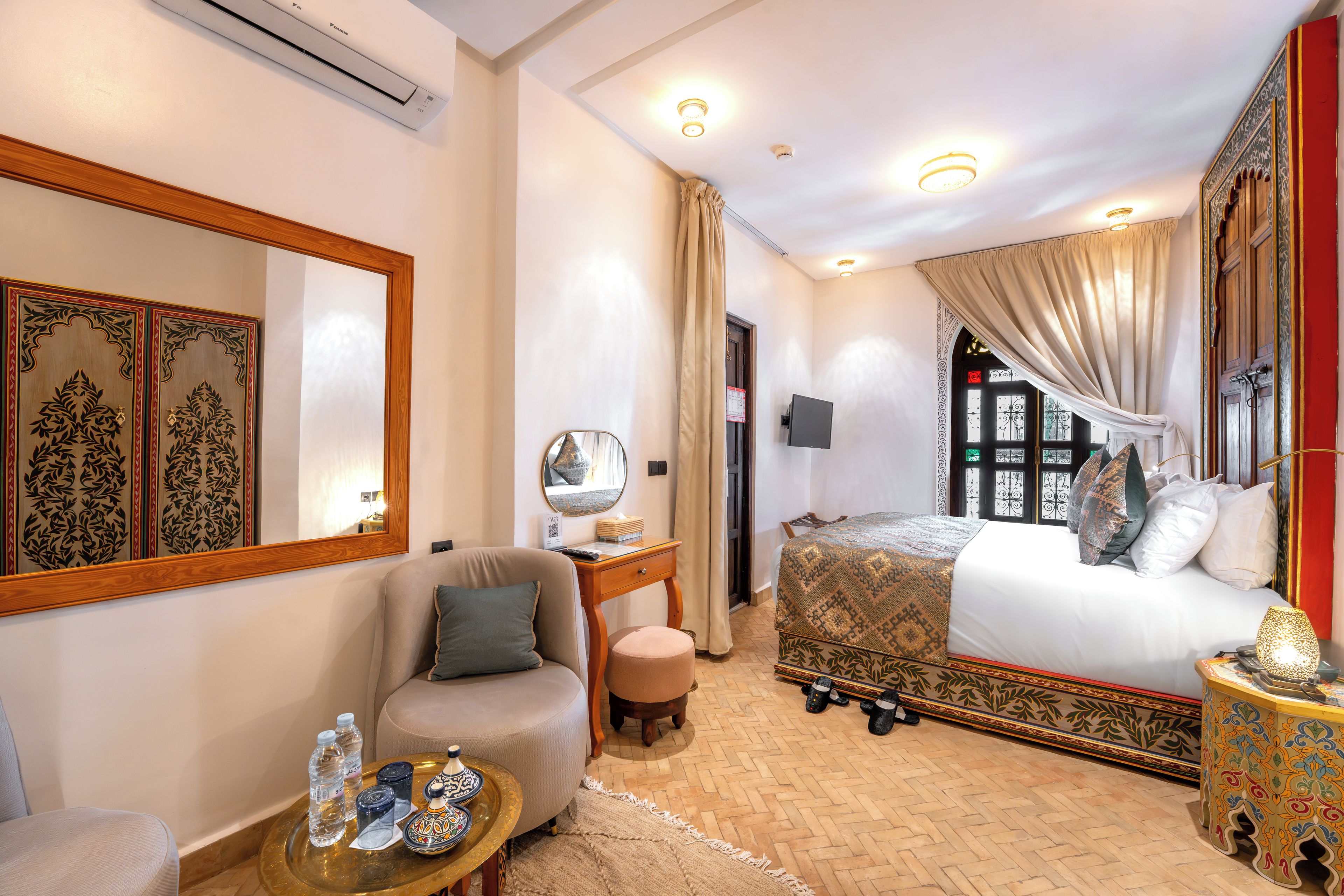 Une chambre d’hôtel comprenant un lit, un coin salon avec un canapé et un fauteuil, une petite table avec un plateau, un miroir et un téléviseur fixé au mur.
