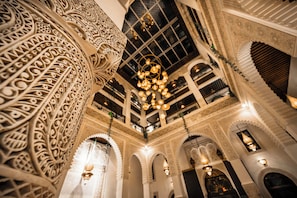 Ein prächtiger Innenraum mit aufwendigen architektonischen Details, darunter geschnitzte Säulen und Bögen, sowie einer zentralen Chandelier.