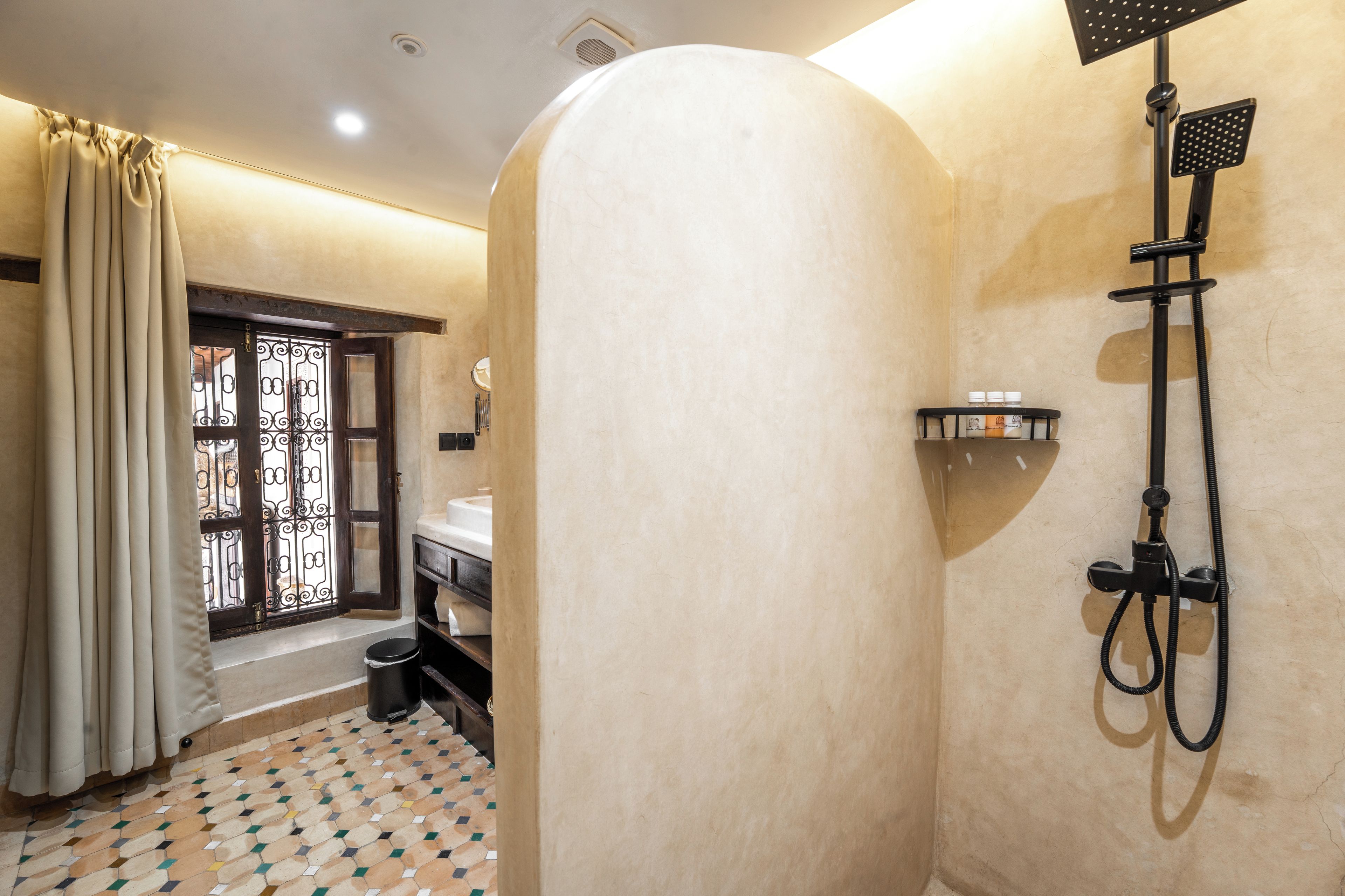A bathroom with a shower, a toilet, a sink, and a window with decorative iron bars.