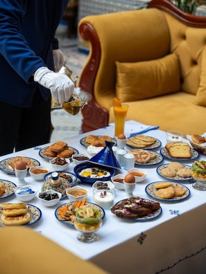A table set with various breakfast items, including pastries, fruits, and beverages, in a room with a sofa and a patterned tablecloth.
