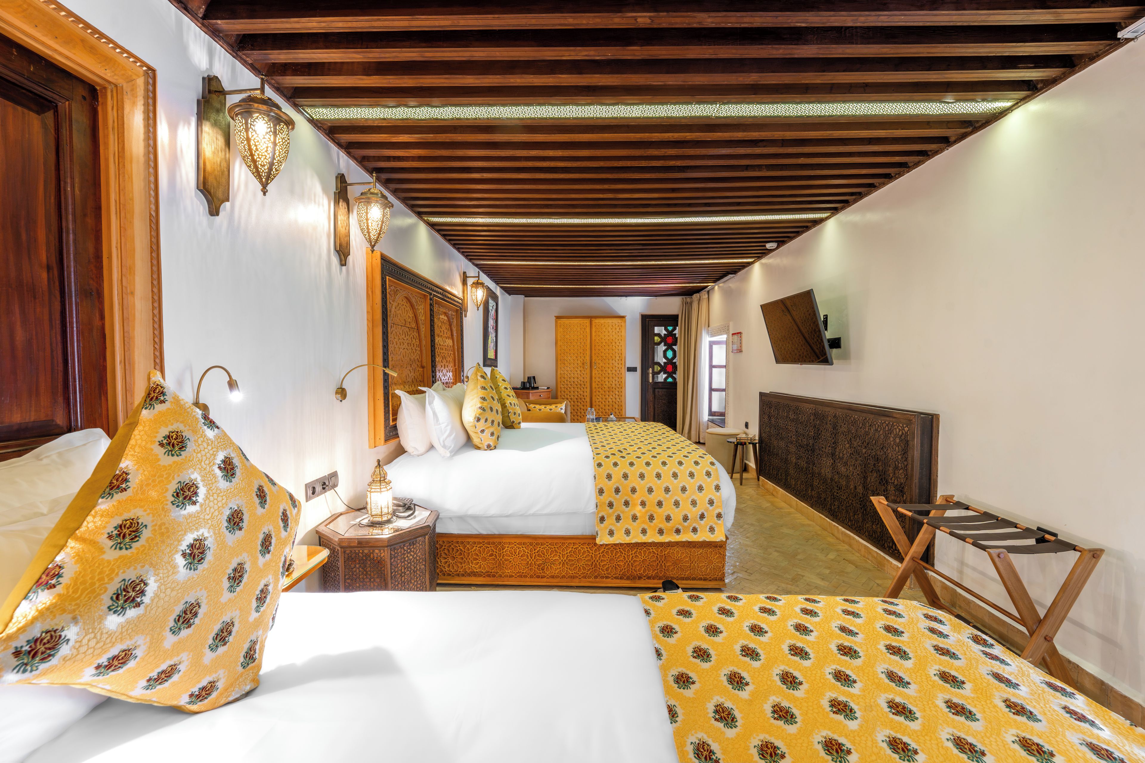Ein Hotelzimmer mit Holzboden, einem Bett mit gemustertem Überwurf, einem Nachttisch mit Lampe und einem kleinen Holzstuhl.