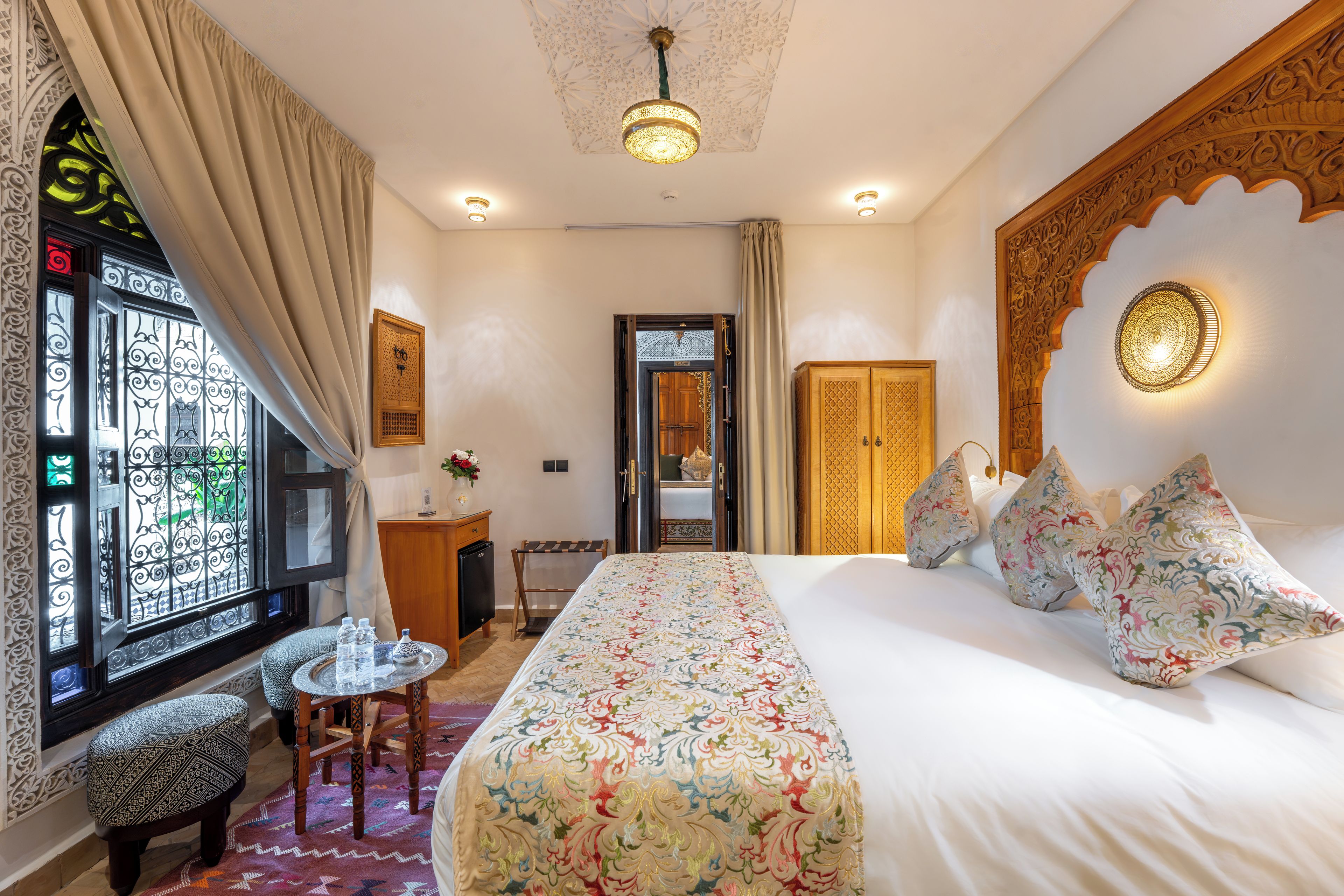 A hotel room with a bed, a desk, a chair, a small table, and a decorative wall.