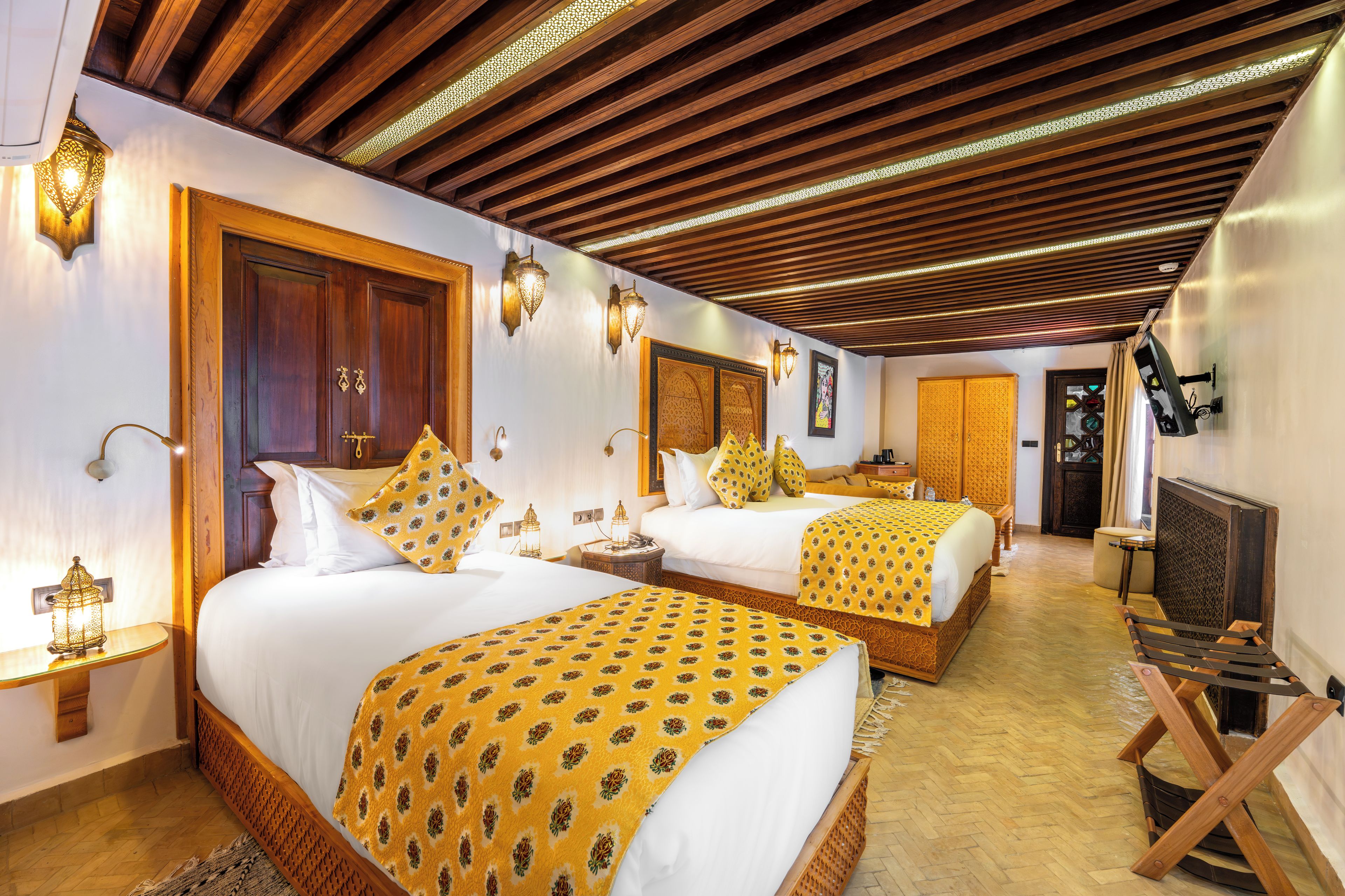 A hotel room with two beds, wooden headboards, and a herringbone-patterned ceiling.