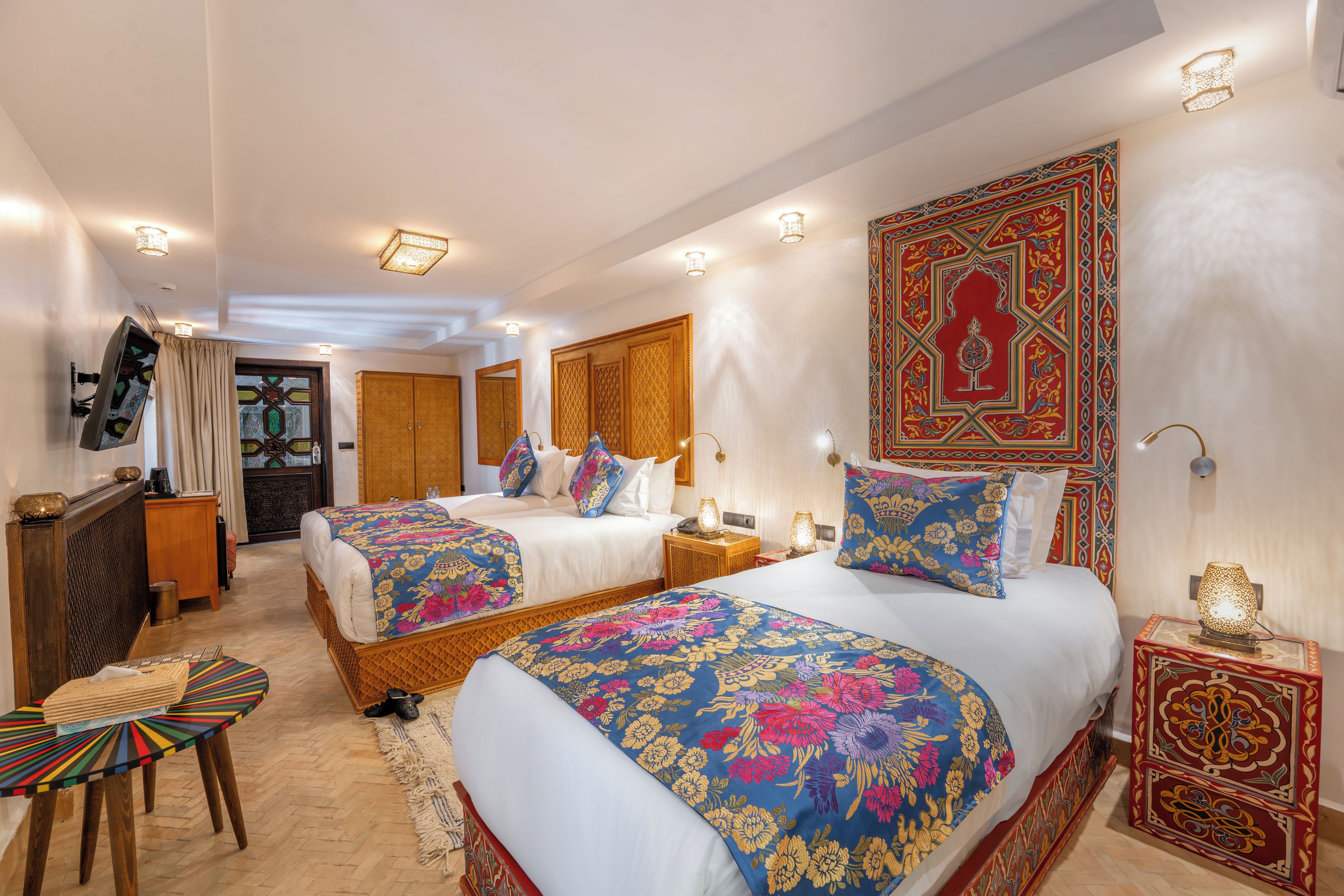 A hotel room with two beds, a sitting area with a chair, a small table, and a decorative wall piece.