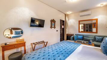 Habitación de hotel con cama, televisión, espejo, mesita de noche de madera, sofá y una mesita con bandeja.