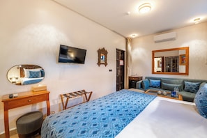 Une chambre d’hôtel comprenant un lit, une télévision, un miroir, une table de chevet en bois, un canapé et une petite table avec un plateau.