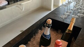 Uma área de bar com garrafas de champanhe em gelo, copos alinhados e uma cozinha moderna ao fundo.