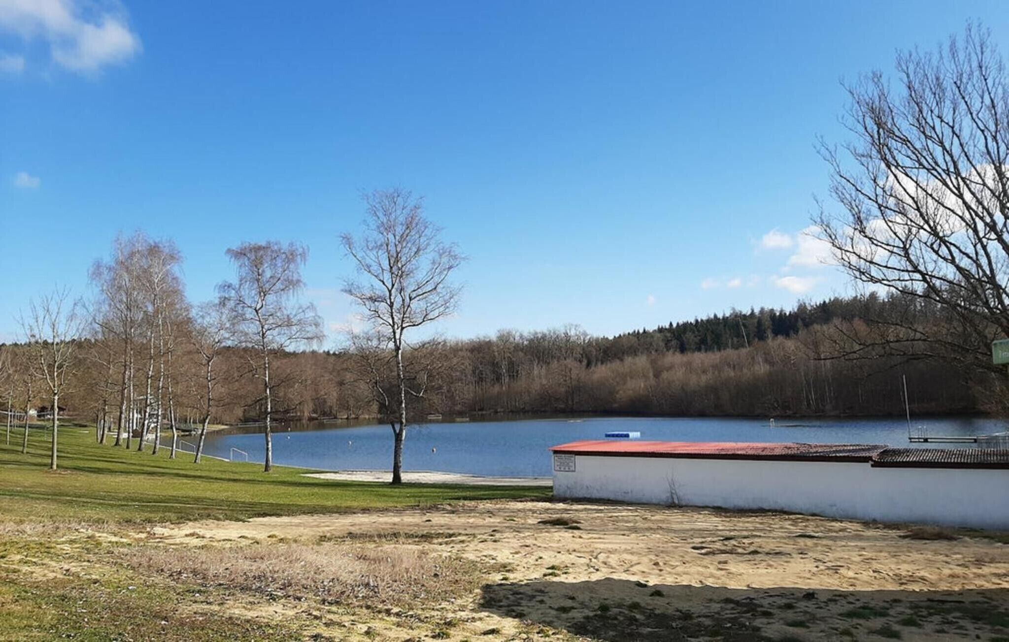 A lakeside view with a small building, trees, and a clear sky.