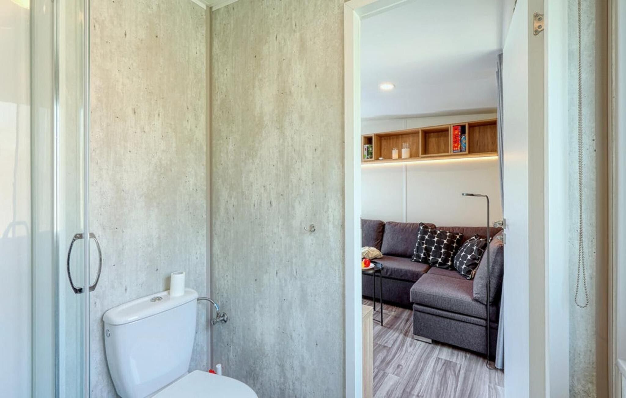 Une salle de bain avec des toilettes, une douche et un mur en béton. On y trouve également un espace de vie avec un canapé et une lampe.