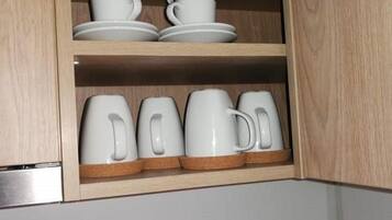 A kitchen cabinet with white ceramic cups and saucers on the upper shelf and white mugs on the lower shelf.