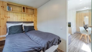 A bedroom with a bed, a wooden headboard, a built-in shelf, and a view of a kitchen and bathroom through a glass door. - Apartment 'Wemding' with Shared Terrace, Private Garden and Air Conditioning (Wemding)