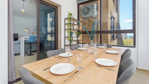 Un coin repas avec une table en bois dressée pour quatre personnes, une cloison en verre et une vue sur l’extérieur.
