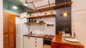 A compact kitchen with white cabinets, a wooden countertop, and a built-in gas stove. There are shelves above the counter holding potted plants and kitchen items.