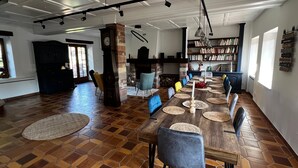 Un vaste espace dédié à la salle à manger, avec une longue table en bois, de nombreuses chaises, une cheminée et une bibliothèque remplie de livres.