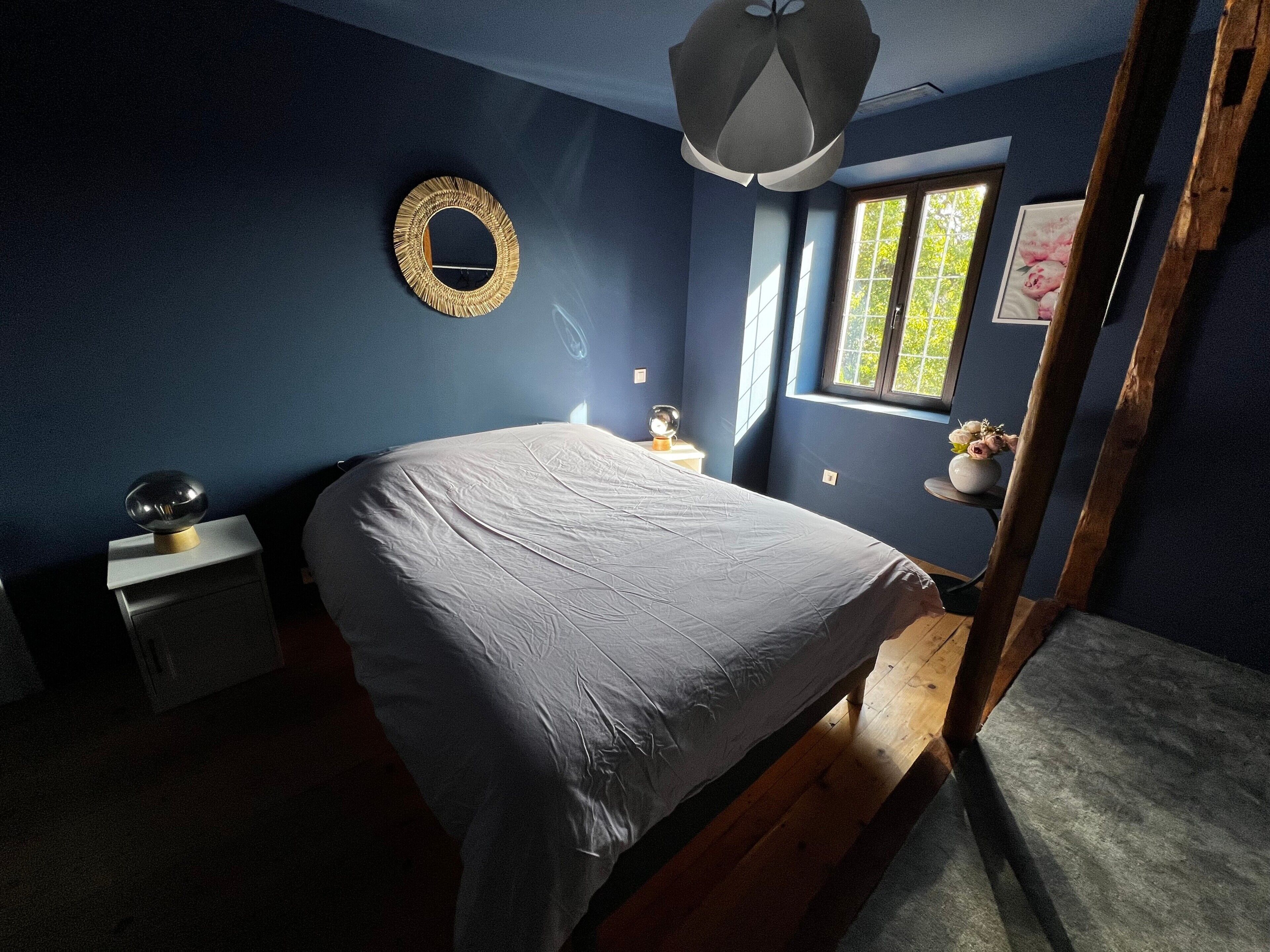 Une chambre à coucher avec un lit, une table de chevet, un miroir, une fenêtre et une échelle en bois.