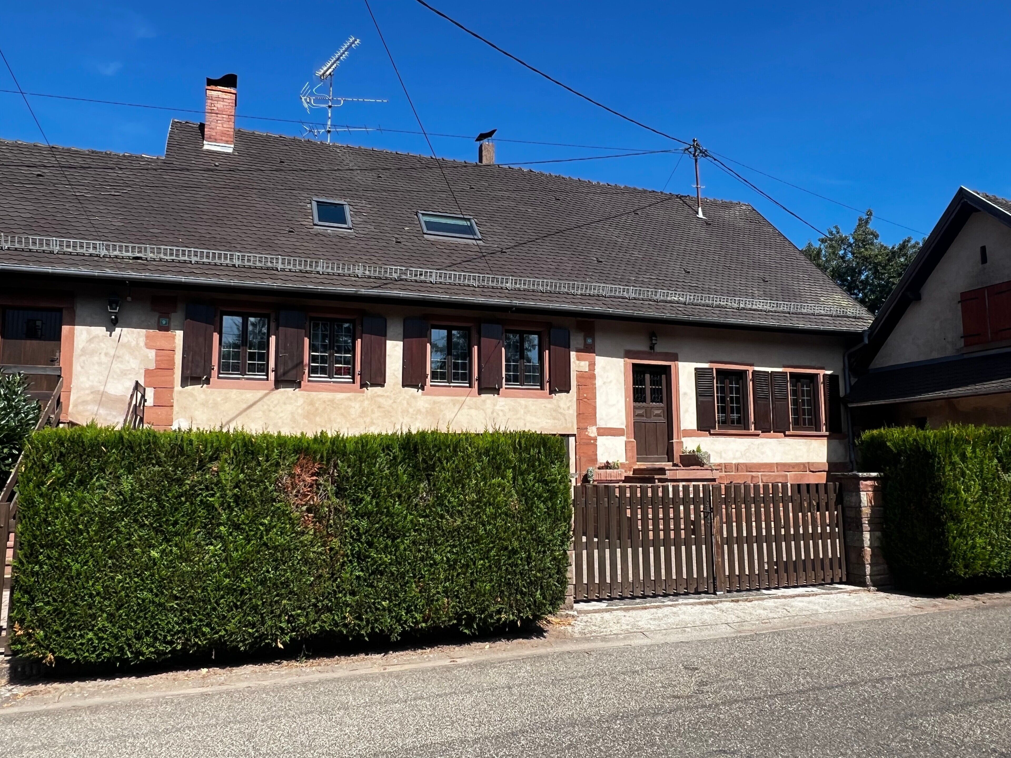 Una casa a due piani con tetto spiovente, recinzione in legno e siepe curata.